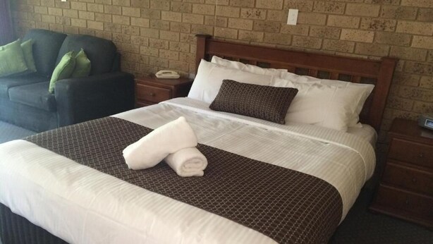 Una cama bien hecha con ropa de cama blanca y marrón, un cabecero de madera y una mesita de noche con una lámpara.