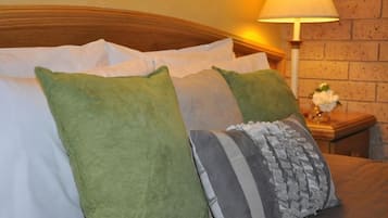 Una cama bien hecha con almohadillas blancas y verdes, una almohada a rayas y un cabecero de madera.