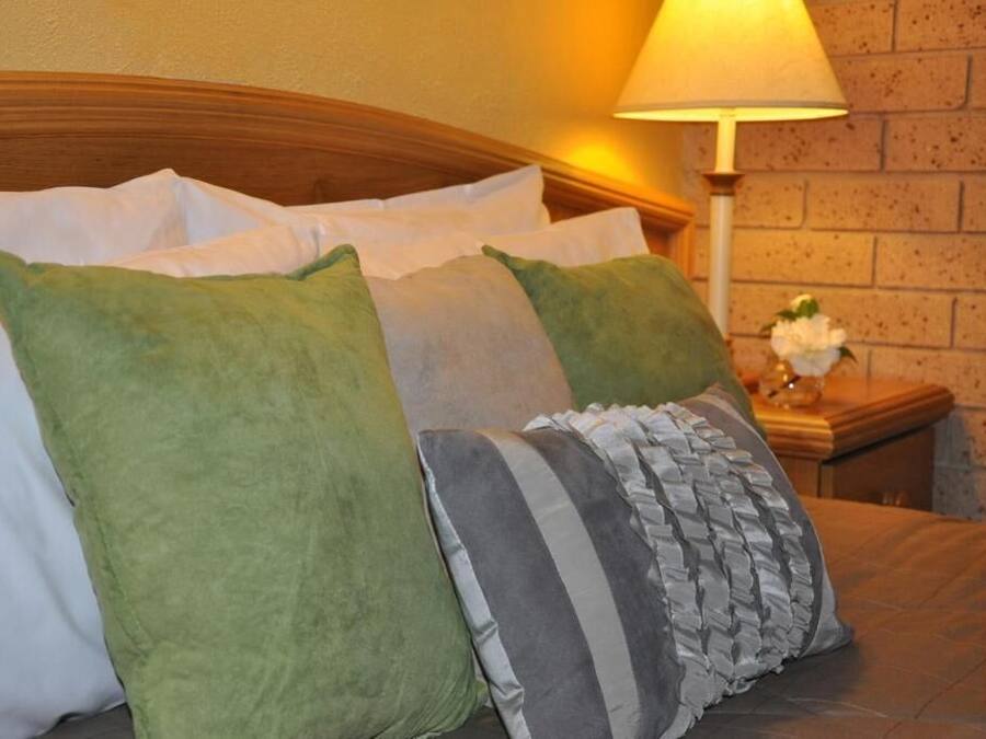 Una cama bien hecha con almohadillas blancas y verdes, una almohada a rayas y un cabecero de madera.