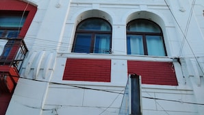A white building with red shutters, multiple windows, and a visible door. - Hostal al Fin del Mundo (Punta Arenas)