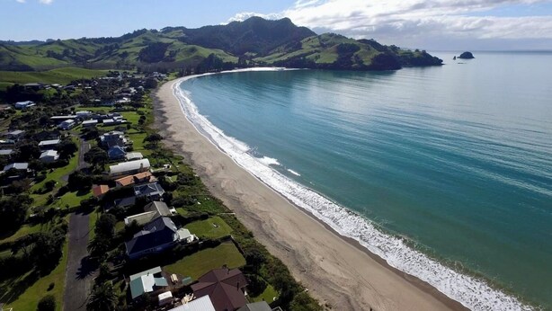 A coastal residential area with houses along the beach, a clear view of the sea, and green hills in the background. - Back to Basics at Iconic Wharekaho Bay (Simpsons Beach) Whitianga (Wharekaho)