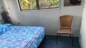 A bedroom with a bed, a chair, a window, and a wall-mounted shelf. - Back to Basics at Iconic Wharekaho Bay (Simpsons Beach) Whitianga (Wharekaho)