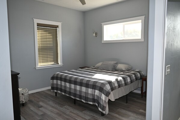 A bedroom with a bed, two windows, a nightstand, and a dresser. - Spacious 4-bedroom house in charming Council with WiFi, AC, 80% ADA compliant. (Council)