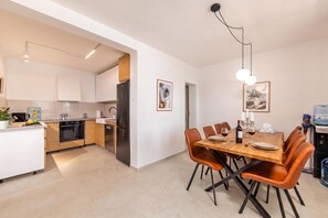 A modern kitchen with a dining area, featuring a stainless steel refrigerator, wooden cabinets, and a dining table with chairs.