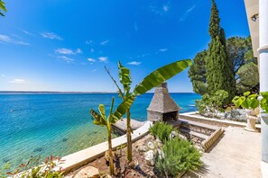 A coastal view with a clear blue sea, a stone structure, and lush greenery.
