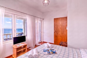 A hotel room with a large window, a bed with a plaid bedspread, a wooden nightstand, a TV, and a wooden door.