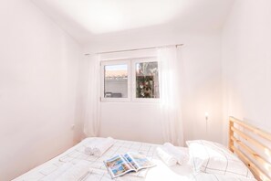 A bedroom with a bed, two pillows, a window, and a magazine on the bed.