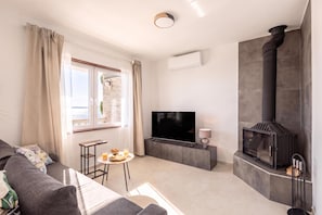 A modern living room with a sofa, a TV, a small table with drinks, a fireplace, and a window with curtains.