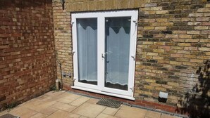 A brick wall with a white-framed door and a tiled patio. - City Apartment Sleeps 4 with Garden (Romford)