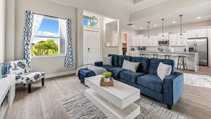 A modern living room with a blue sofa, white coffee table, and a view of the kitchen. - Sleeps 6, Pool, Bicycles, Waterfront: Whispering Sapphire (Cape Coral)