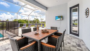 A covered patio with a wooden table and wicker chairs, a pool, and a view of the sky and palm trees. - Sleeps 6, Pool, Bicycles, Waterfront: Whispering Sapphire (Cape Coral)