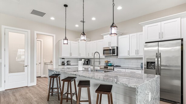 A modern kitchen with white cabinets, a stainless steel refrigerator, a marble island with bar stools, and pendant lighting. - Sleeps 6, Pool, Bicycles, Waterfront: Whispering Sapphire (Cape Coral)