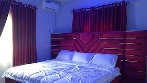 A bedroom with a large bed, red curtains, and a wall-mounted air conditioner.