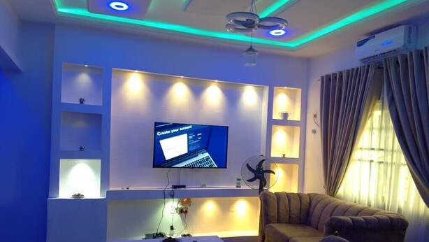 A modern living room with a flat-screen TV mounted on the wall, a ceiling fan, and a sofa.