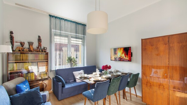Una sala de estar moderna con un sofá azul, una mesa de comedor preparada para cuatro personas y una estantería llena de libros.