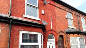 A red brick house with white-framed windows, a satellite dish, and a door marked with the number 24. - MCRShared House-Big Bedroom Sleeps 3 (Manchester)