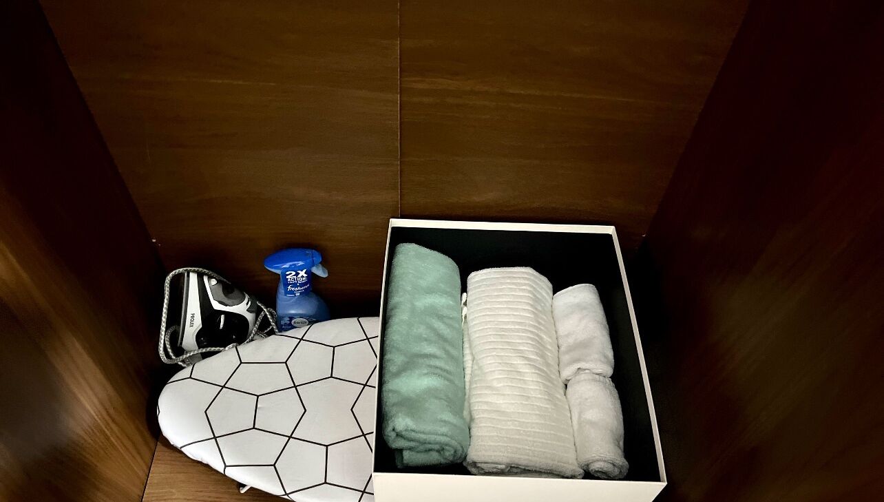 Un placard contenant une boîte de rangement blanche dans laquelle se trouvent des serviettes pliées et une bouteille d’eau bleue.