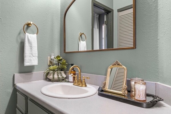 A bathroom with a white sink, gold faucets, a mirror with a gold frame, and a small plant on the counter.