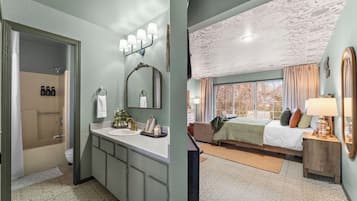 Een badkamer met douche, wastafel en badkamermeubel, en een slaapkamer met bed, dressoir en uitzicht vanuit het raam.