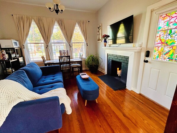 A living room with a blue sofa, a white armchair, a fireplace, and a TV mounted above it.