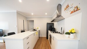 A modern kitchen with white cabinetry, a central island, a black refrigerator, and a stainless steel range hood.