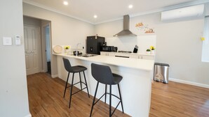 A modern kitchen with a white countertop, two bar stools, a stainless steel sink, and a black refrigerator.