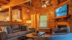 L’intérieur d’un chalet confortable, avec des murs en bois, un canapé, des fauteuils, une table basse et une cheminée.