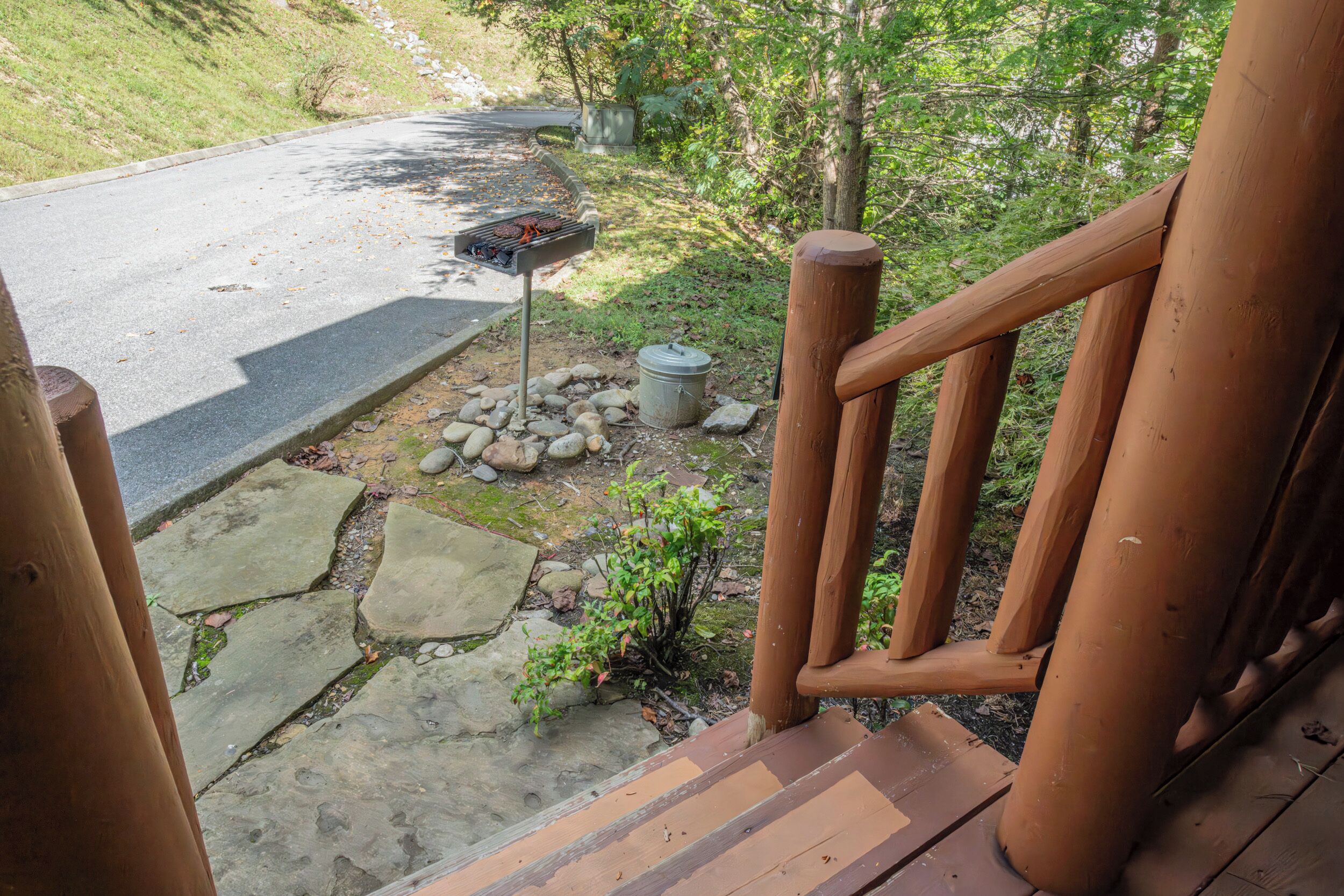Une terrasse en bois avec un barbecue et un récipient en métal, le tout installé sur une surface pavée de pierres.