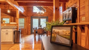 L’intérieur d’un chalet en bois comprend un coin repas, une cuisine et un tableau encadré posé sur un comptoir.