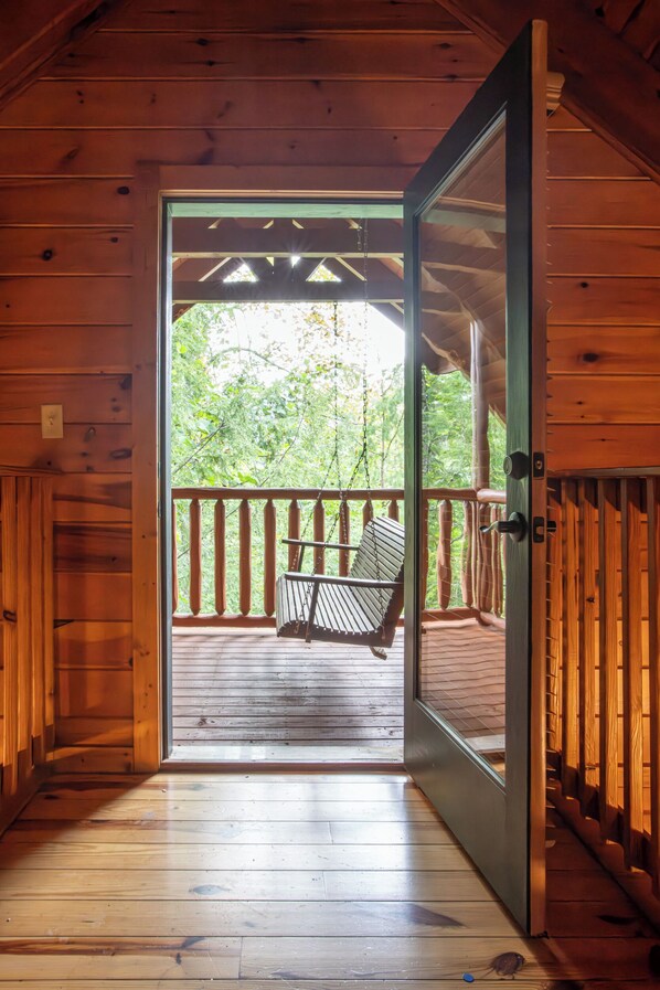 Une cabane en bois avec une véranda, un fauteuil suspendu et une vue sur les arbres.