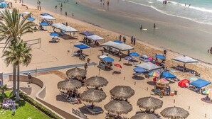 Vue aérienne d’une plage avec des parasols en chaume, des chaises longues et quelques étals installés au bord de la plage.