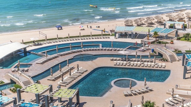Un complexe hôtelier doté d’un grand espace piscine, de plusieurs piscines et d’une plage avec des parasols.