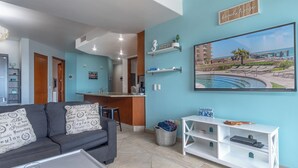 Un salon moderne avec un canapé gris, une table basse et un téléviseur diffusant une scène de plage.