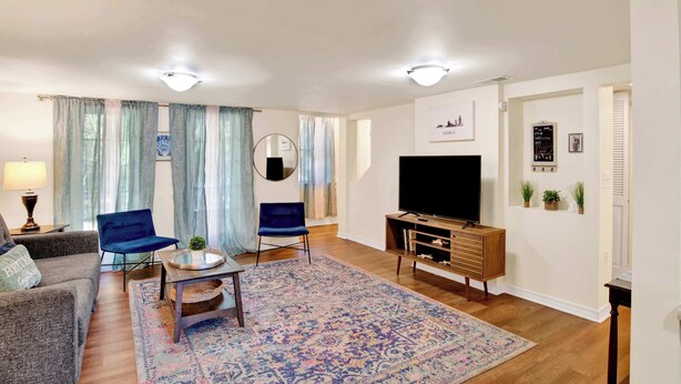 A living room with a sofa, two blue chairs, a coffee table, a TV, and a wooden entertainment unit. - Near Downtown and Cornerstone - Southern Sunshine (Mobile)