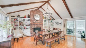 A spacious loft with a high ceiling, exposed wooden beams, a brick fireplace, and a large dining table surrounded by chairs. - 10 Mi to Crane Beach: Wooded Home Near Boston! (Topsfield)