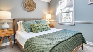 Ein Schlafzimmer mit einem Bett, zwei Nachttischen, einer Wandlampe, einem Fenster mit Jalousien und einer Wanddekoration.