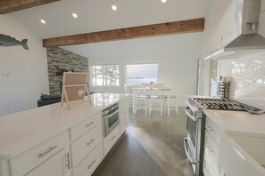A modern kitchen with white cabinetry, a stone accent wall, and a view of the water. - Waterfront Roque Bluffs Hideaway w/ Private Beach (Roque Bluffs)