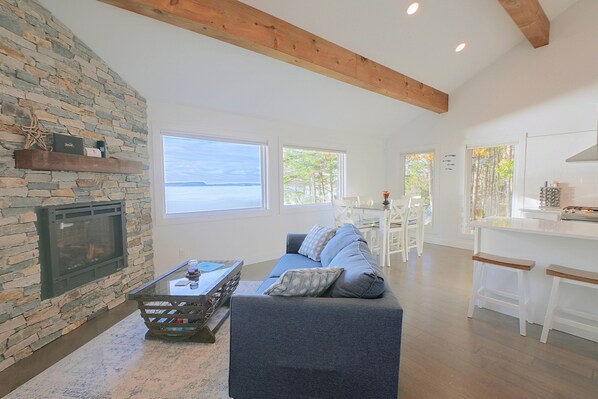 A spacious living area with a stone wall, a fireplace, a sofa, and a view of the sea. - Waterfront Roque Bluffs Hideaway w/ Private Beach (Roque Bluffs)