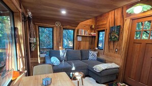 Interior acogedor de una cabaña con techo de madera, un sofá, una mesa de comedor y una silla.