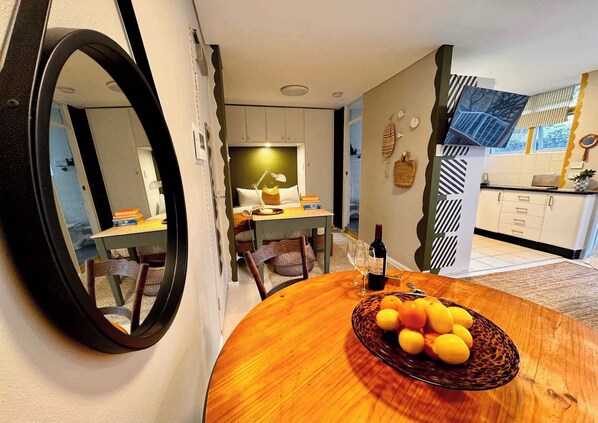 A dining area with a round wooden table, a mirror, and a view into the kitchen.