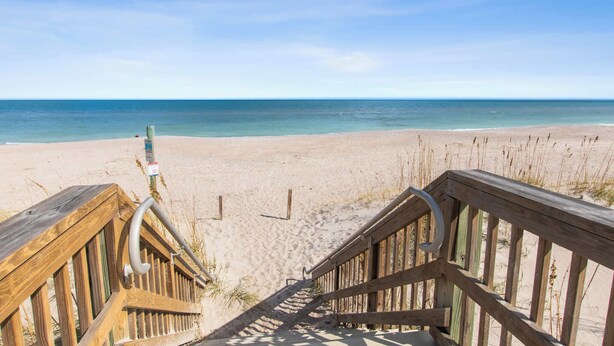 A wooden staircase leading to a sandy beach with a clear view of the ocean.