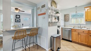 A kitchen with a built-in washer and dryer, a bar area with wicker chairs, and a ceiling fan.