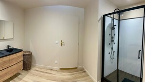 A modern bathroom with a double sink vanity, a glass shower enclosure, and a curved door. - Beautiful renovated apartment in the countryside (CABANNES)