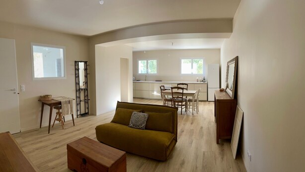 A modern living room with a sofa, a wooden chest, and a dining area with a table and chairs. - Beautiful renovated apartment in the countryside (CABANNES)