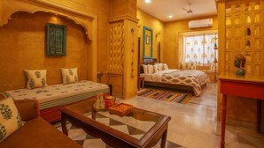 A traditional room with a sofa, a bed, a small table, and a decorative cabinet. - Bhimkothi (Jaisalmer)