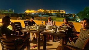 A group of people dining outdoors at night with a historic building in the background. - Bhimkothi (Jaisalmer)