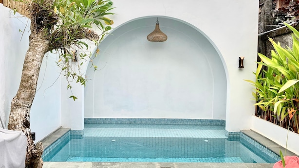 Pequena piscina com azulejos, parede branca e entrada em arco.