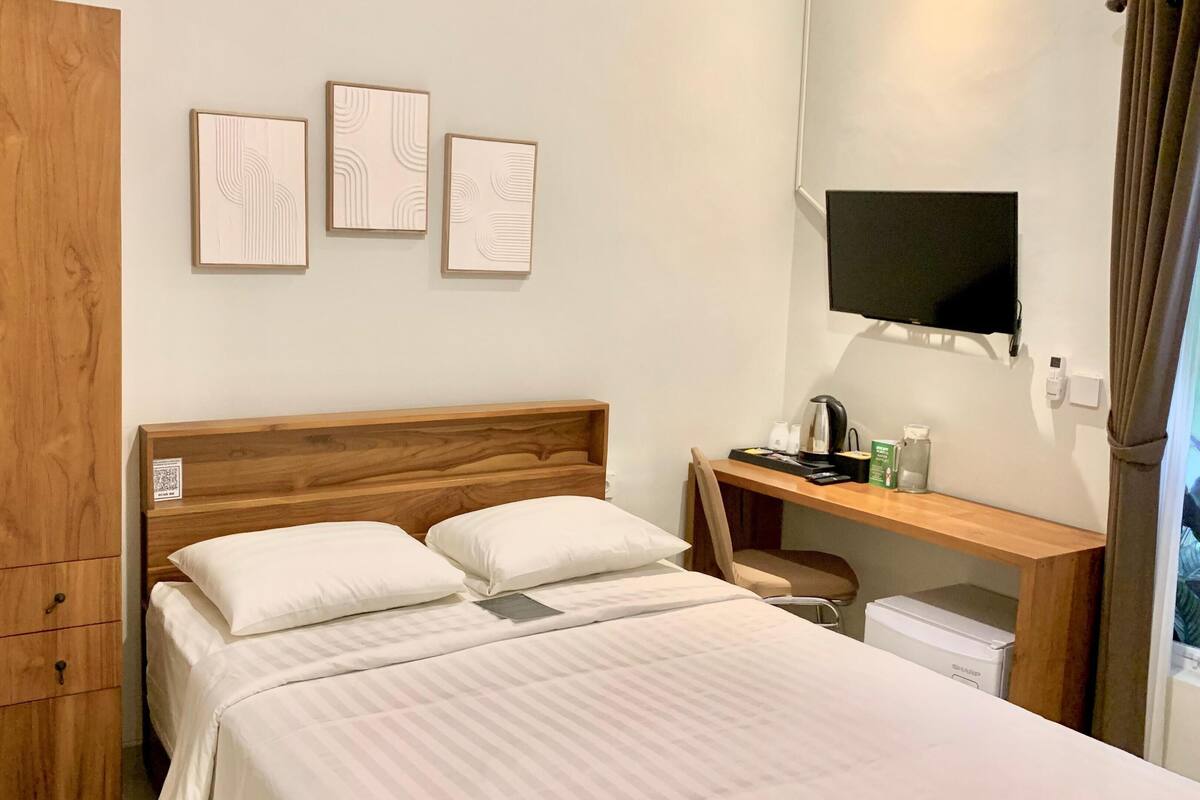 A hotel room with a wooden bed, a desk with a flat-screen TV, and a wardrobe.
