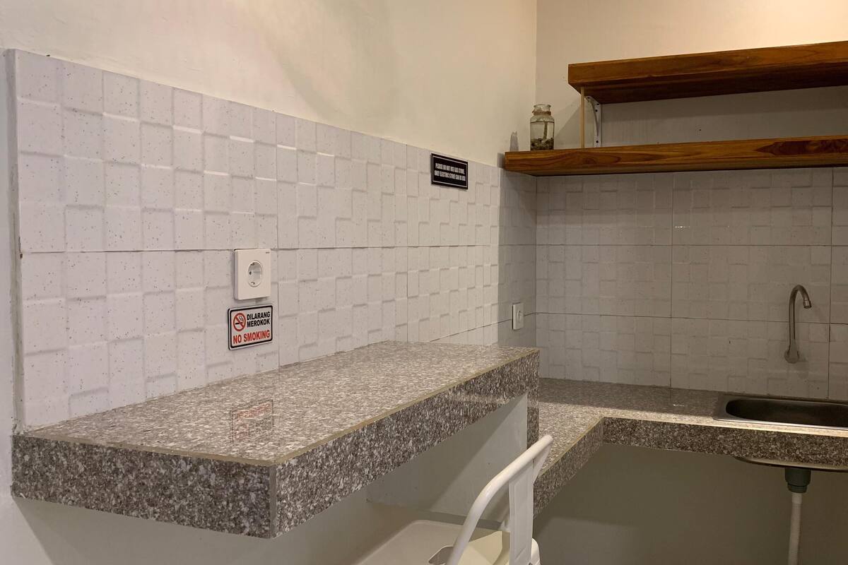 A small kitchen with white tiled walls, a granite countertop, a wooden shelf, and a no smoking sign.