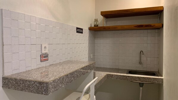 A small kitchen with white tiled walls, a granite countertop, a wooden shelf, and a no smoking sign. - Baliem Boutique Hotel Ungasan (Jimbaran)